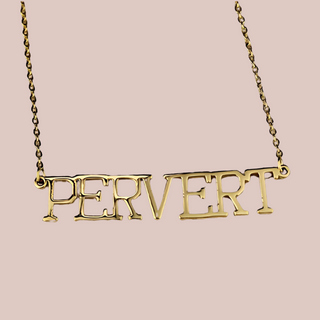 A close up view of the Pervert necklace, you can see the capital letters, gold colouring and the chain.